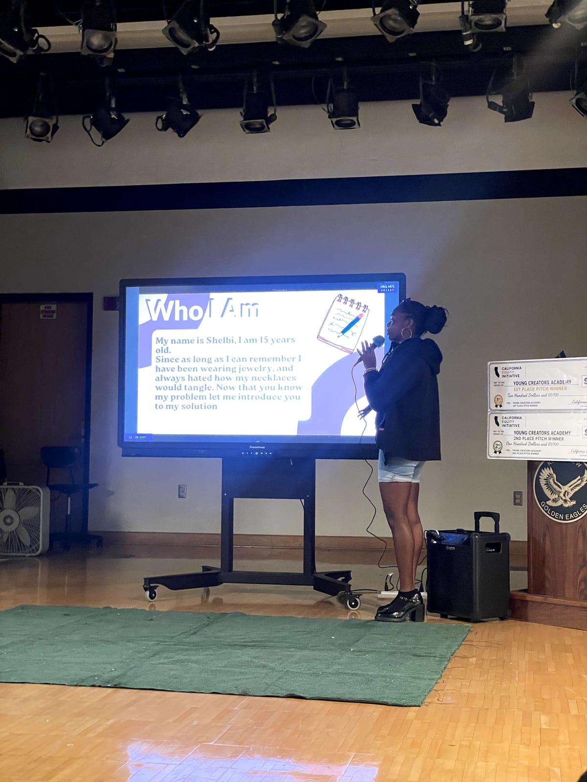 A student pitching her product idea on stage beside the prize checks