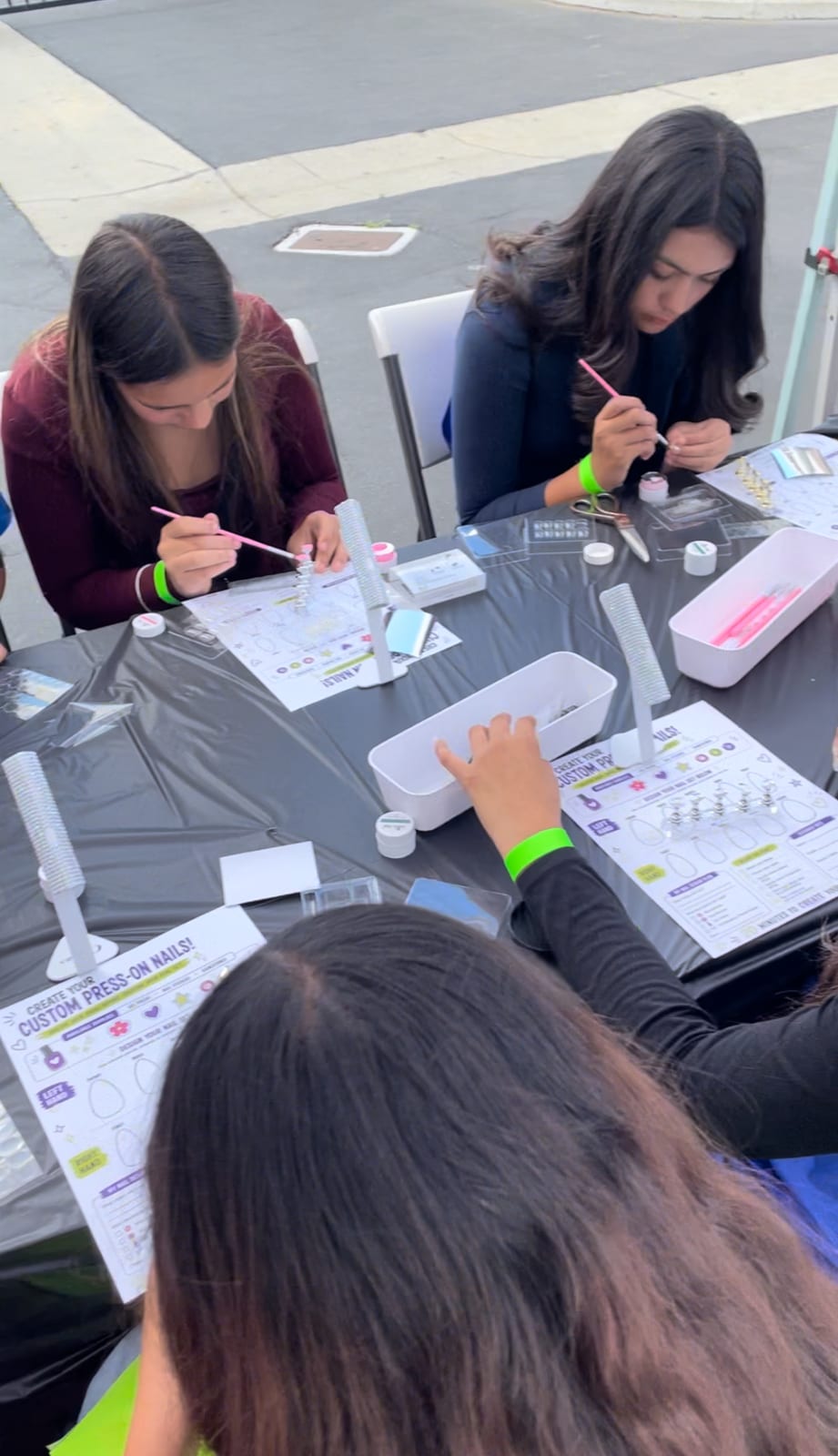Students painting their own custom press-on nails at an outdoor workshop table