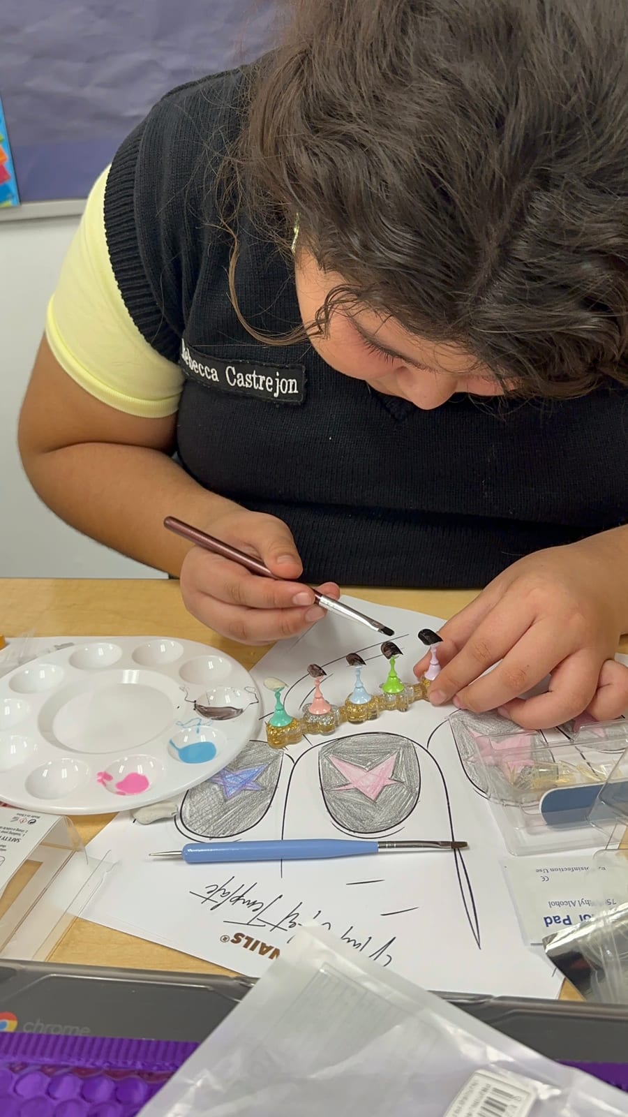A student hand-painting a set of press-on nails from her own design sketch